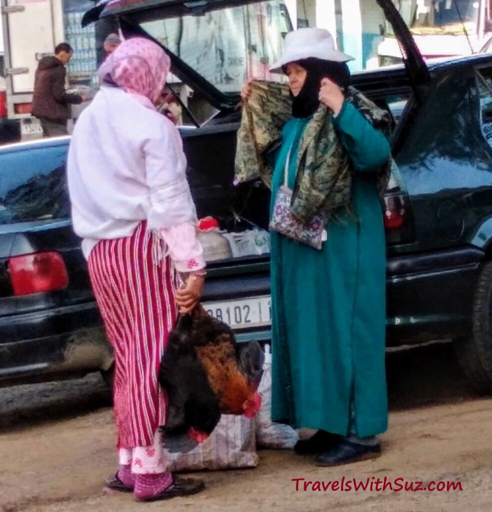 Two women in the souk gossiping; one holding a chicken by the legs